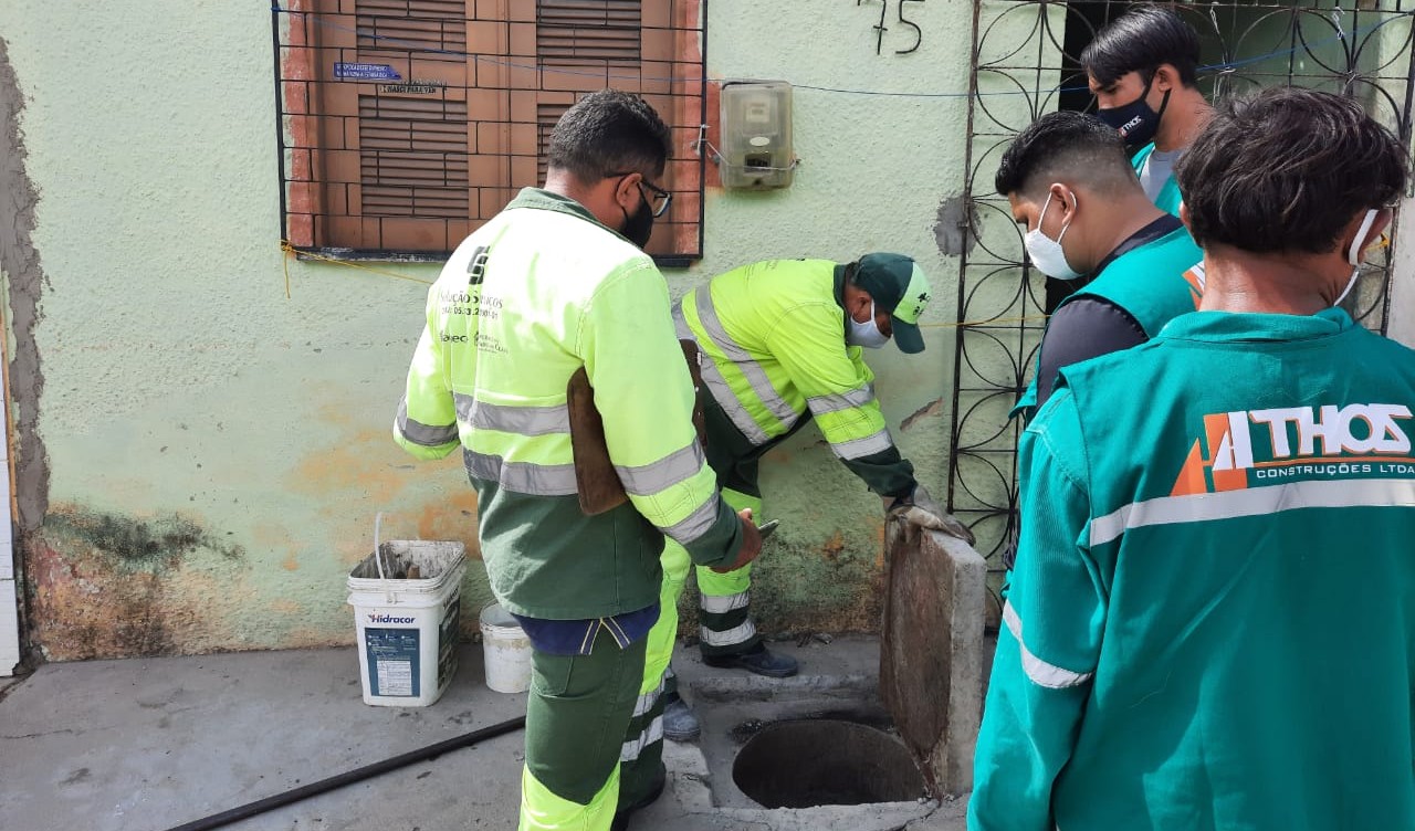 Um grupo de quatro homens examina uma tampa de esgoto na frente de uma residência